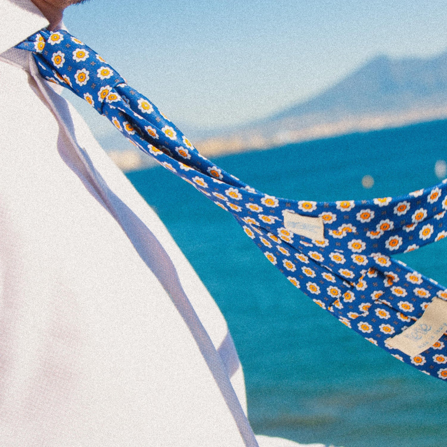 Un uomo che contempla il mare e il Vesuvio in una giornata soleggiata e ventosa. L'uomo indossa una camicia bianca e una cravatta TieTiè.