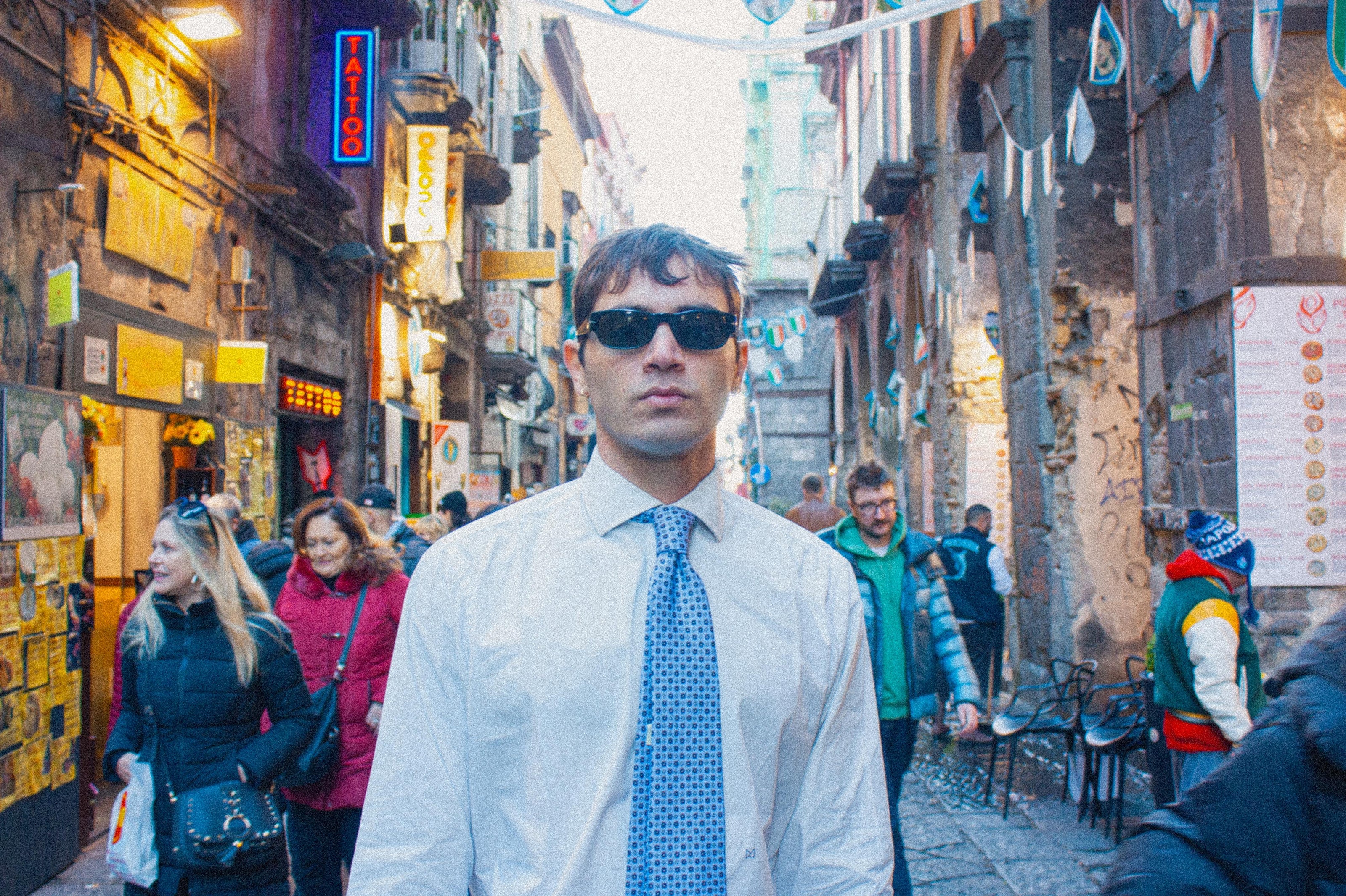 Un uomo che sta andando a lavoto in camicia e cravatta TieTiè. Sta passeggiando per via dei tribunali a Napoli e indossa degli occhiali da sole neri. 